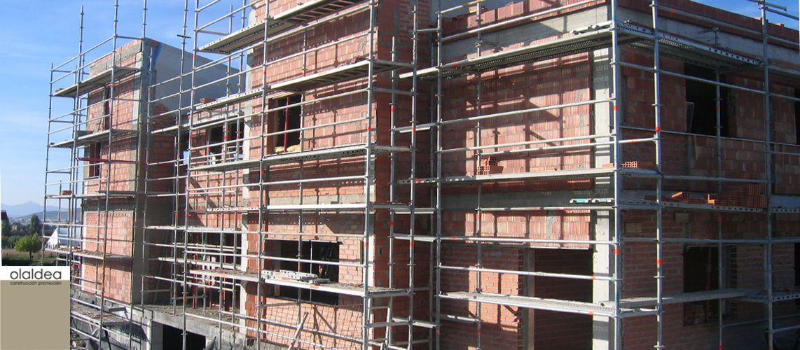 Edificio en construcción con andamios en un día soleado. Estructura de ladrillo y ventanas visibles.
