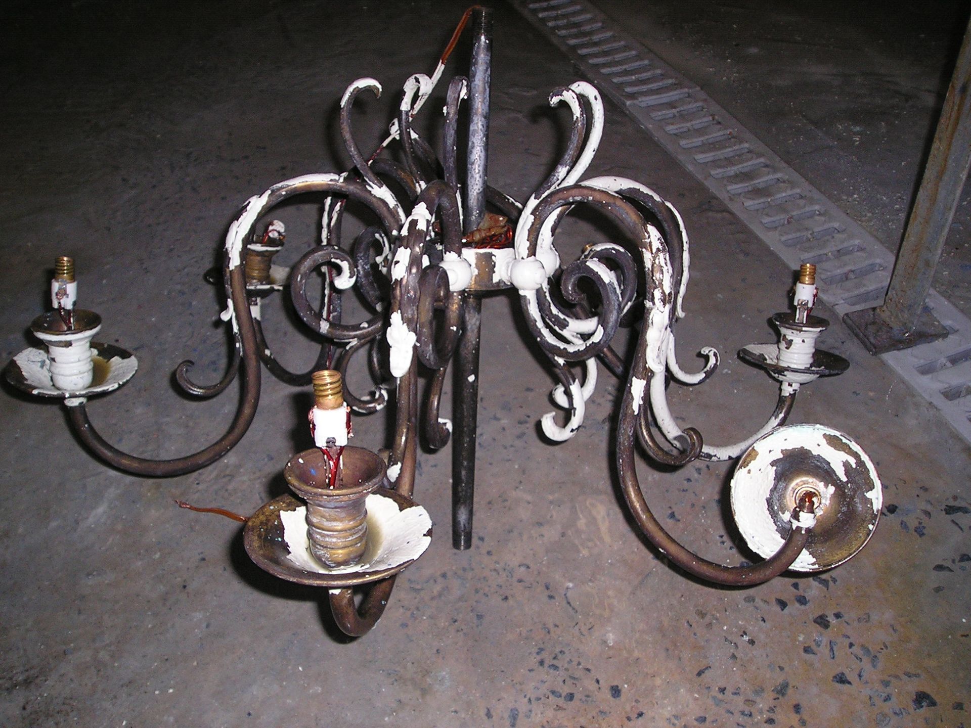 Lustre vintage en fer forgé peint en blanc, à trois douilles, posé sur une surface en béton foncé.