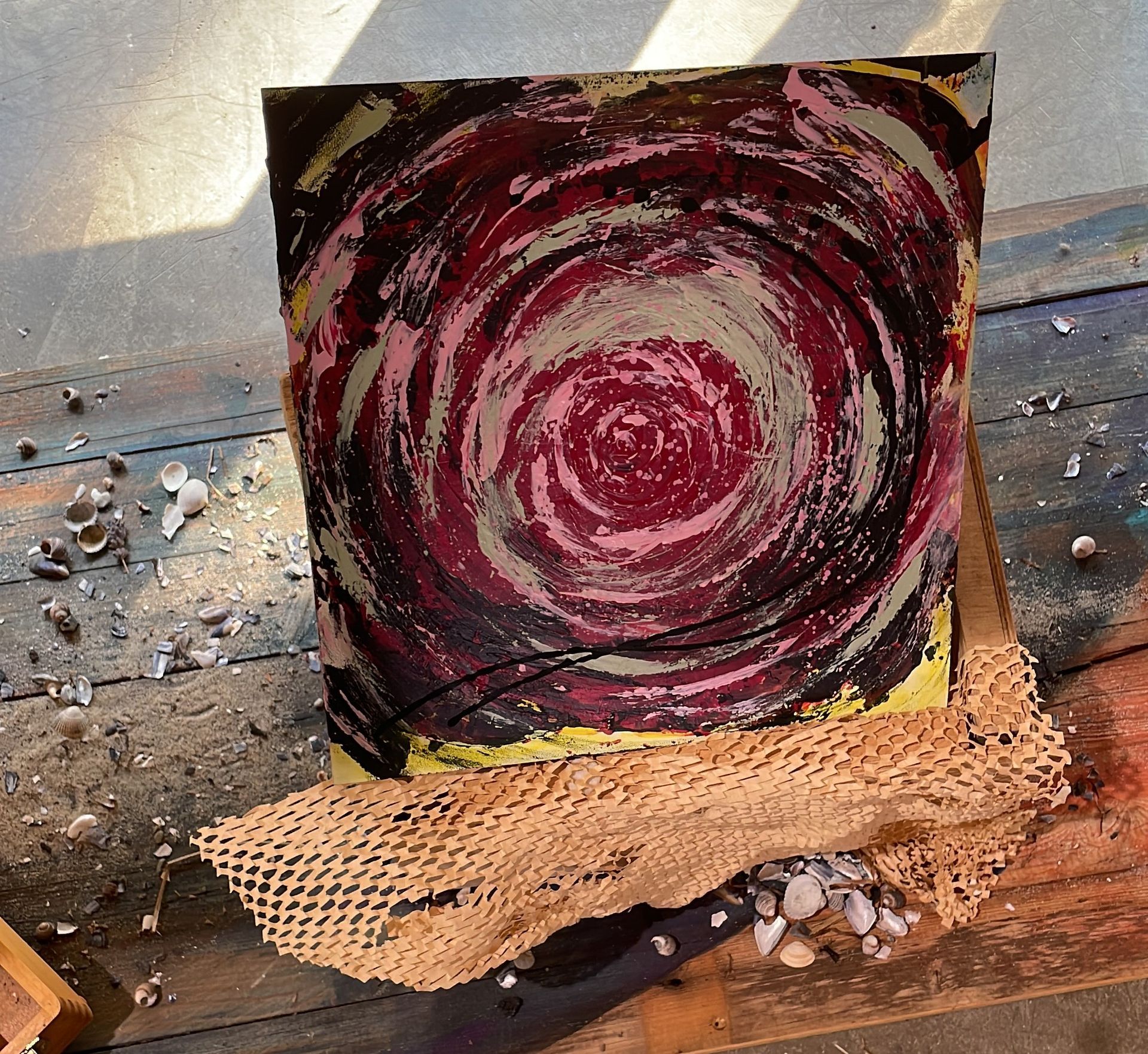 Abstraktes Spiralbild in Rot-, Rosa- und Gelbtönen auf Holz, umhüllt von Papier.