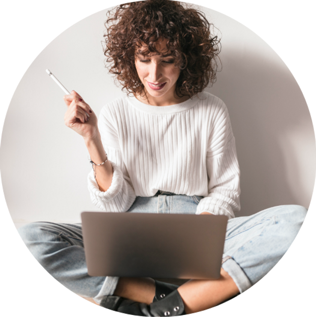 Uma mulher está sentada no chão usando um laptop e segurando uma caneta