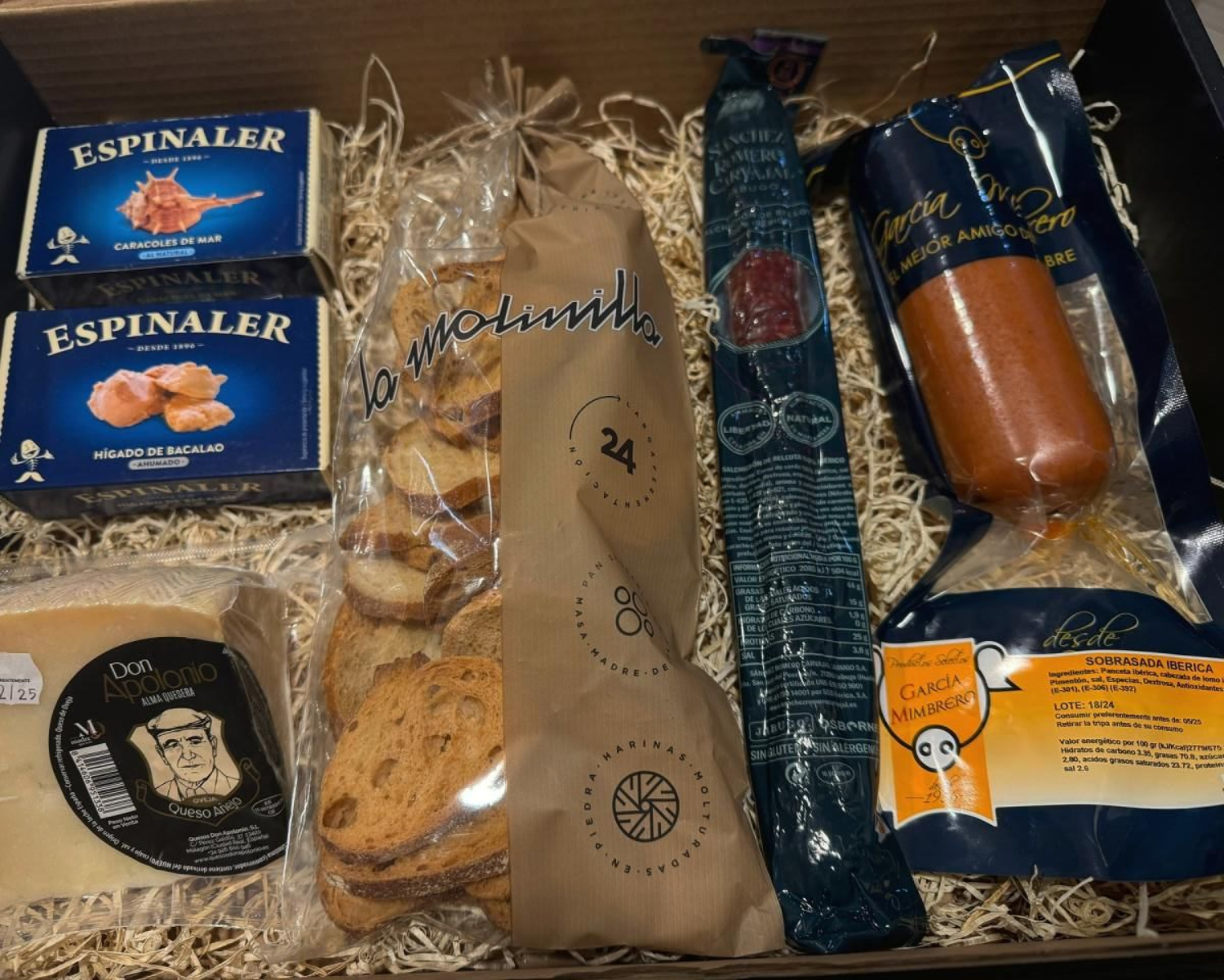Una caja de regalo con alimentos gourmet que incluyen queso, galletas y embutidos.