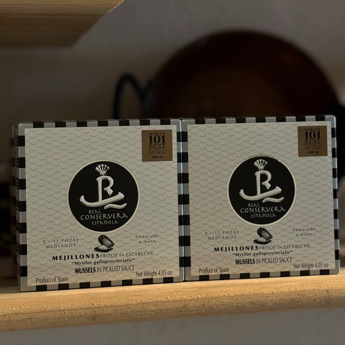 Dos cajas de mejillones Mejillones en una lata decorativa, expuestas en un estante de madera.