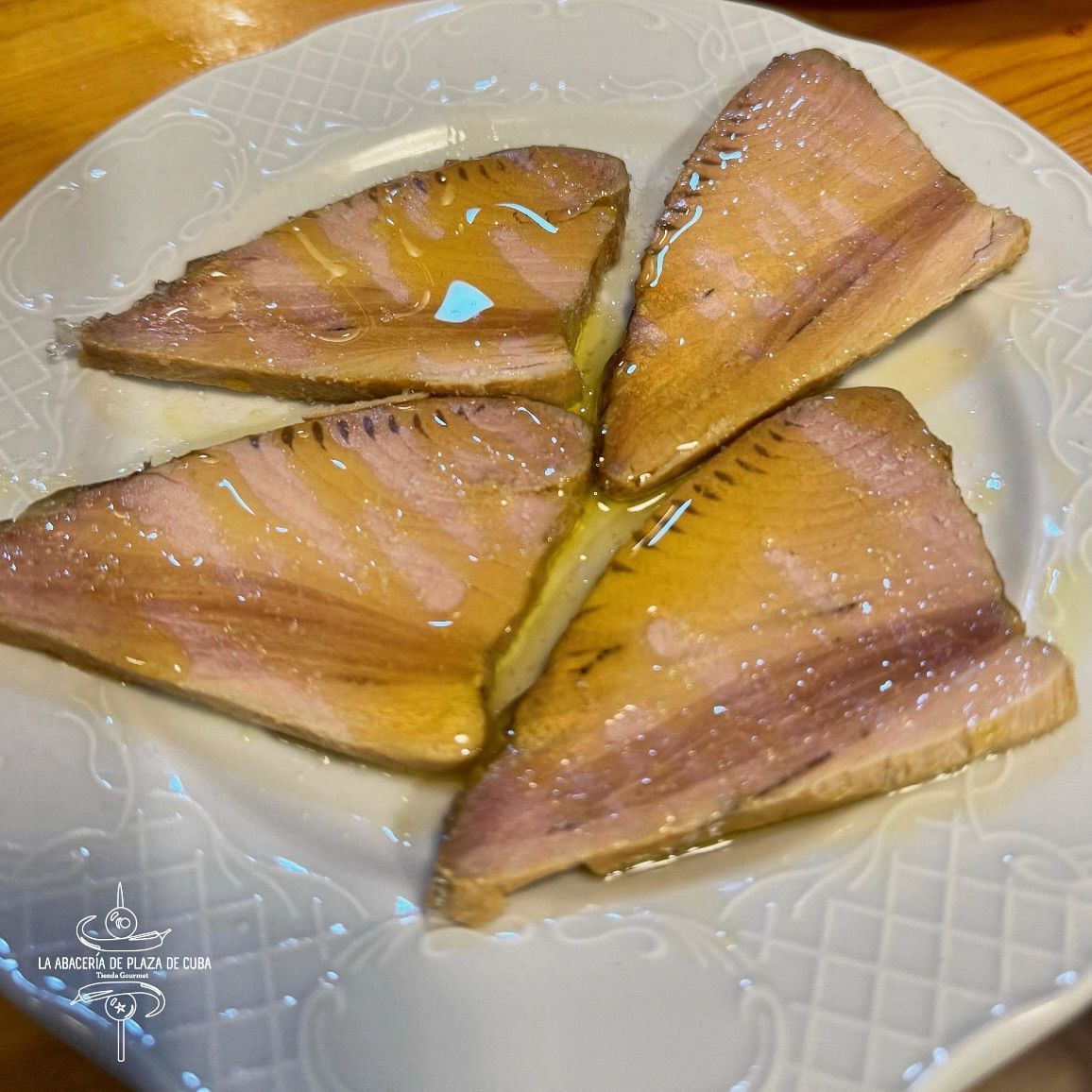 Cuatro trozos de filete de pescado rociados con aceite sobre un plato blanco con borde estampado.