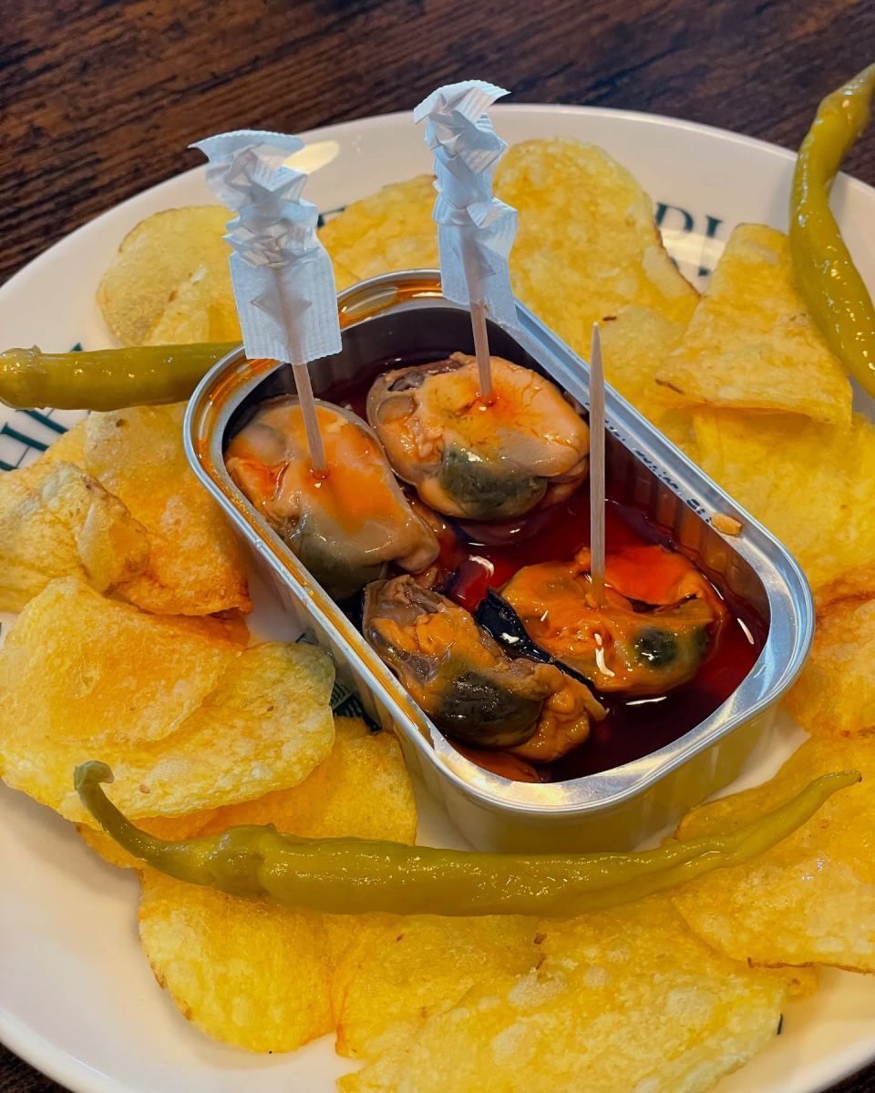 Plato de mejillones en salsa acompañados de patatas fritas y pimientos.