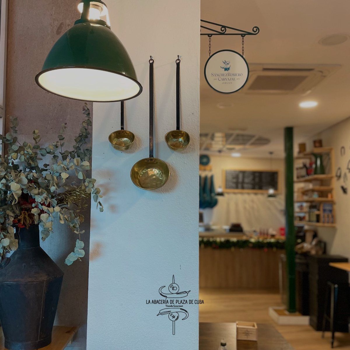 Interior de una cafetería con lámpara verde, cucharones decorativos y cartel.