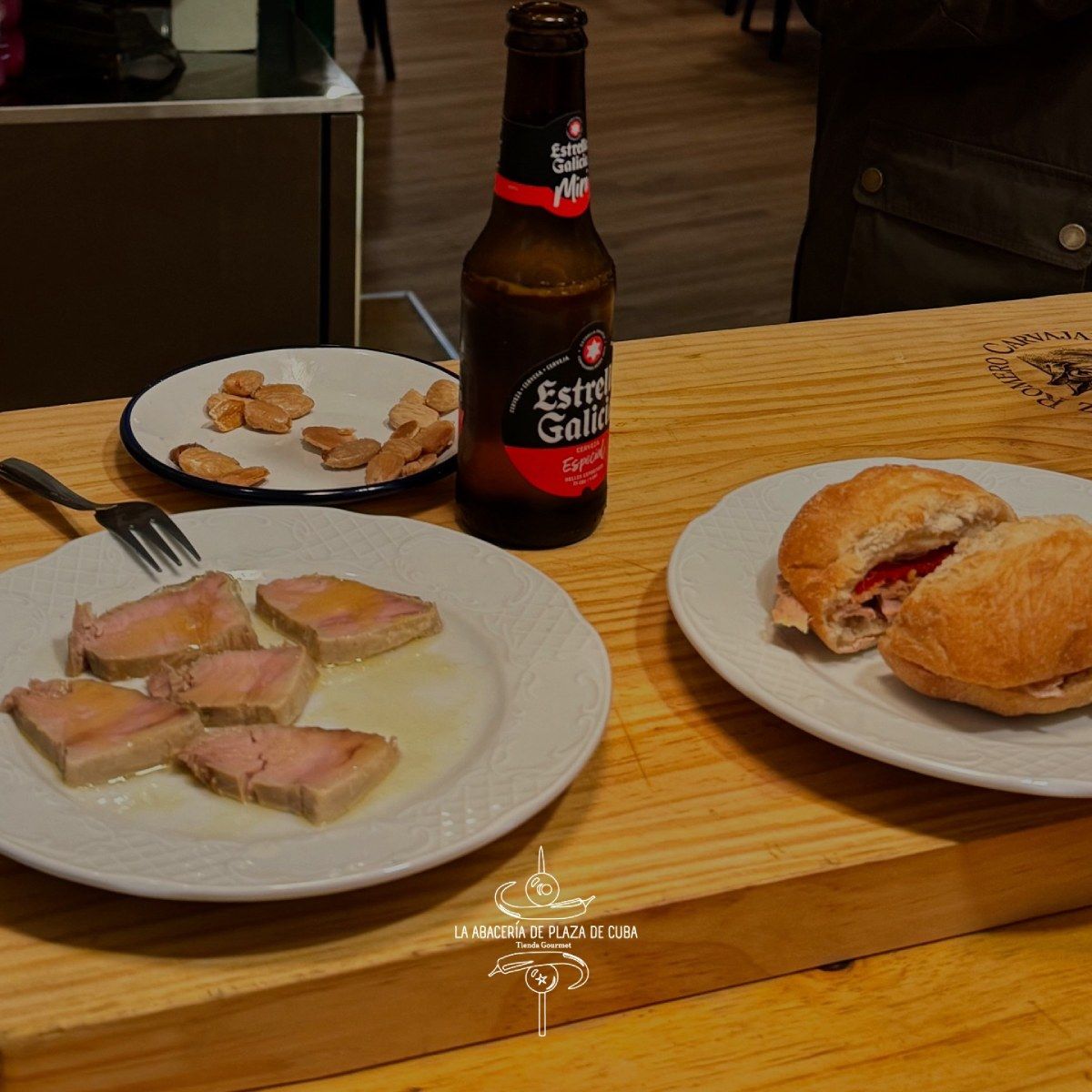 Comida y cerveza en barra: atún, bocadillo, almendras y una botella de cerveza Estrella Galicia.