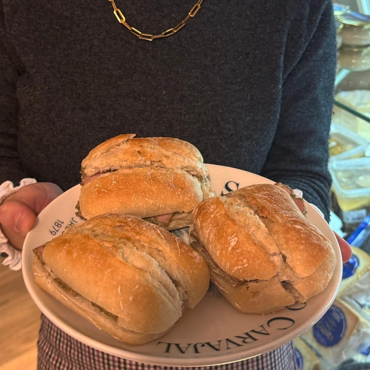 Persona sosteniendo un plato con tres sándwiches. Los sándwiches están en un plato.