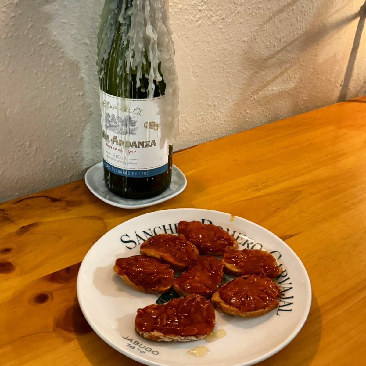 Plato de tapas con una botella de vino cubierta de cera de vela sobre una mesa de madera.