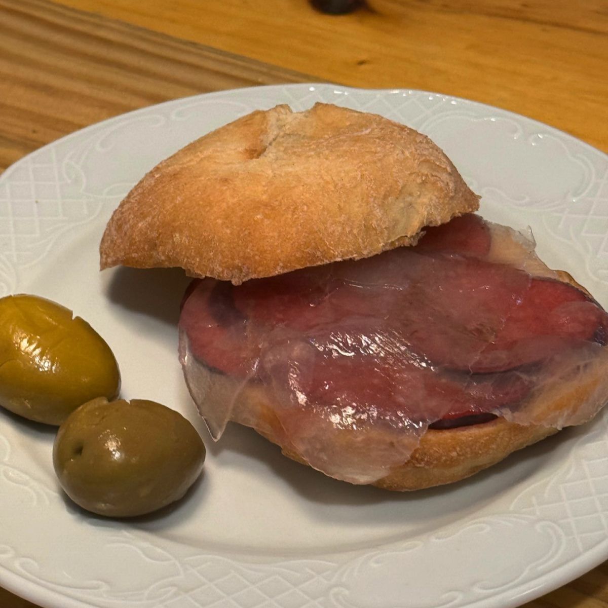 Sándwich de carne y queso en plato blanco, acompañado de aceitunas verdes.