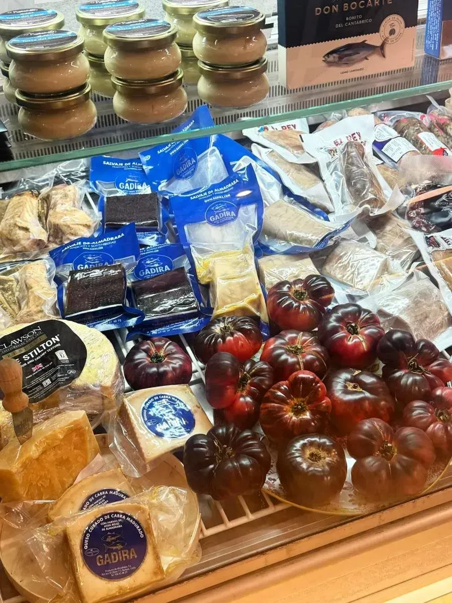 Vitrina con diversos alimentos envasados, entre ellos quesos, tomates y tarros de comida.
