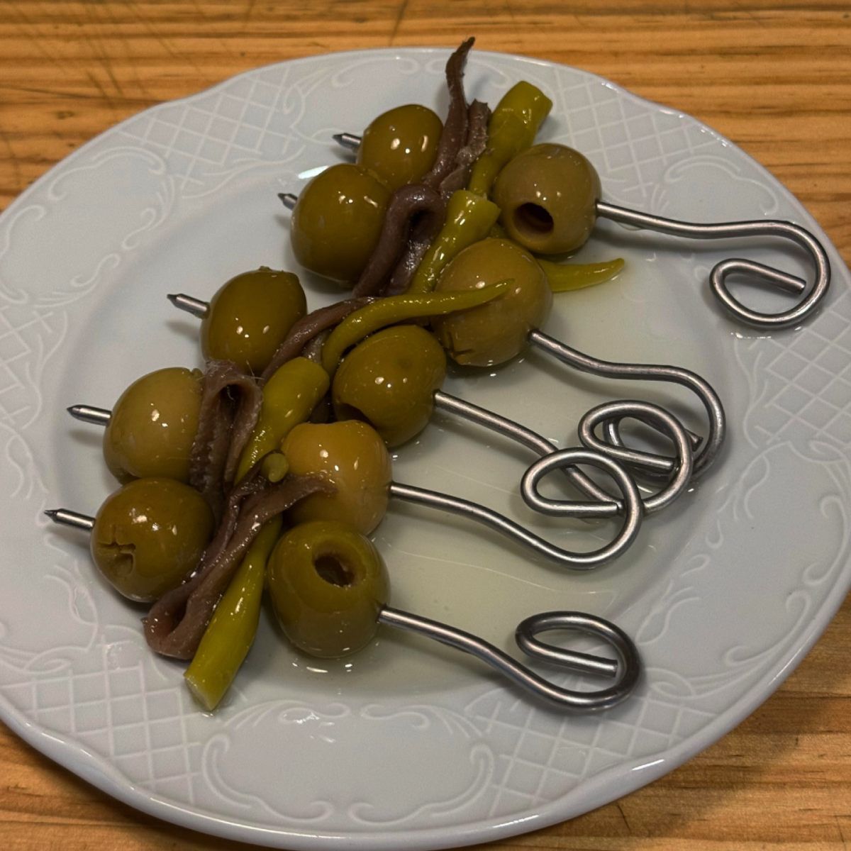 Brochetas de aceitunas verdes con anchoas y pimientos en plato blanco.
