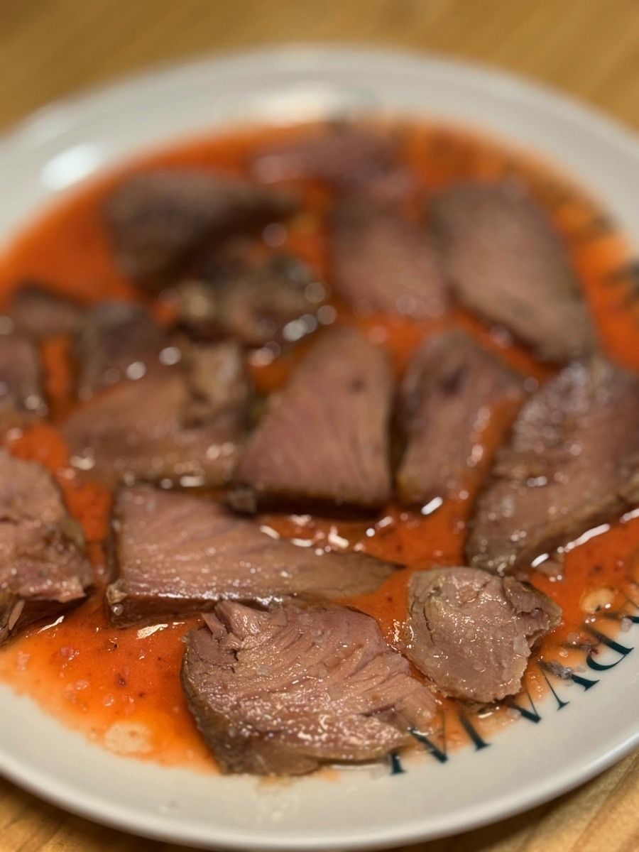 Carne cortada en rodajas en salsa roja en un plato blanco.