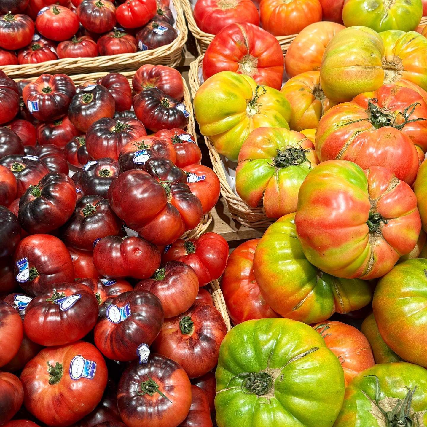 Tomates de varios colores en cestas: rojos, naranjas, verdes y morados oscuros.