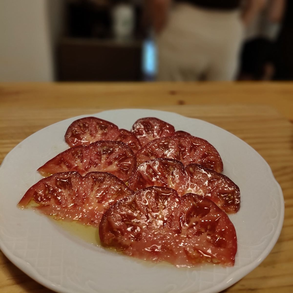 Rodajas de tomates rojos brillantes con salsa en un plato blanco, mesa de madera.