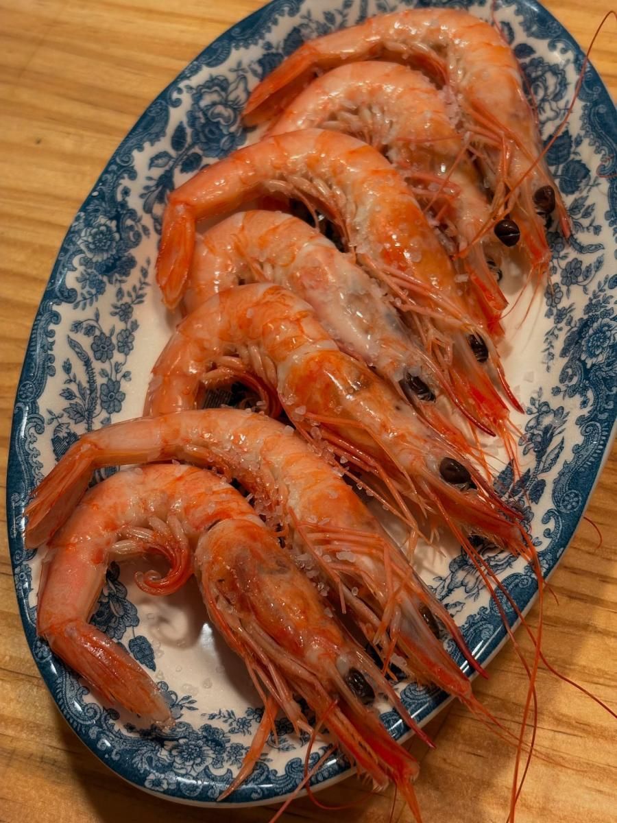Camarones cocidos en un plato ovalado con estampado azul y blanco, sobre una superficie de madera.