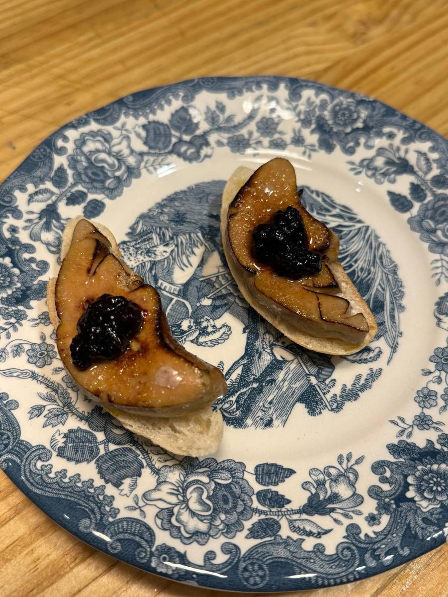 Dos lonchas de foie gras selladas con compota oscura sobre pan tostado, servidas en un plato con estampado azul y blanco.