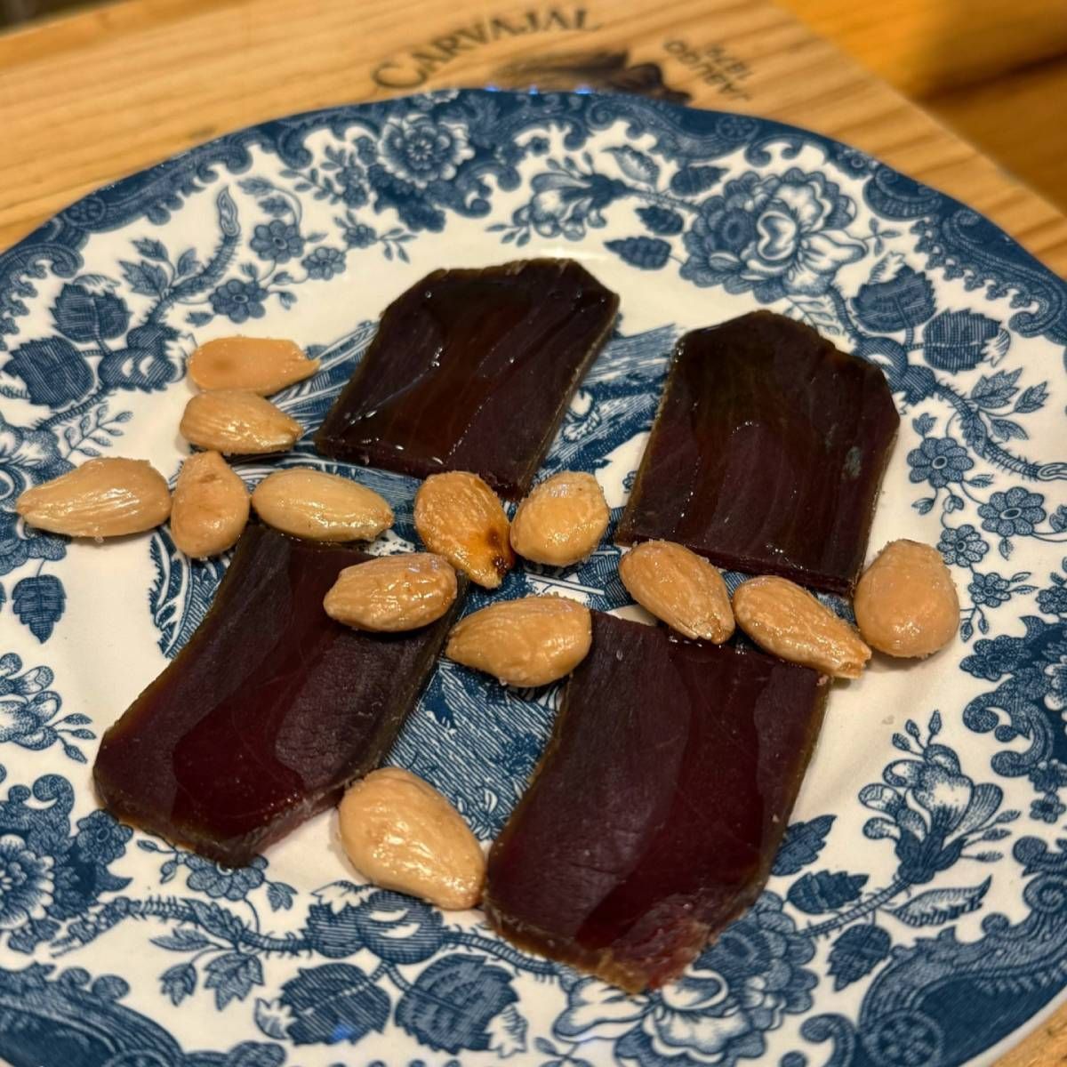 Cuatro rebanadas oscuras de carne con almendras tostadas en un plato con estampado azul y blanco.