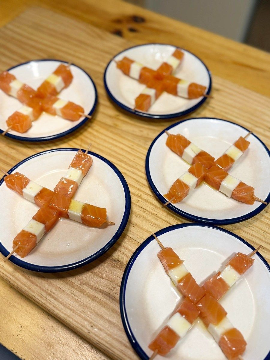 Brochetas de salmón y queso blanco dispuestas en forma de X sobre pequeños platos blancos con bordes azules.
