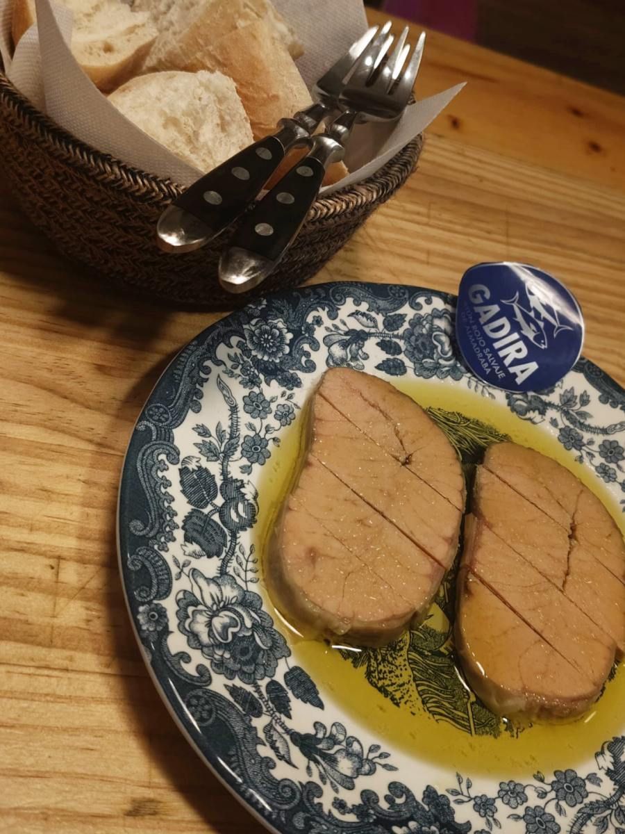 Atún en aceite de oliva en plato estampado, con pan y cubiertos al lado.