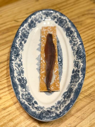 Filete de anchoa sobre una galleta, adornado en un plato ovalado con estampado azul y blanco.