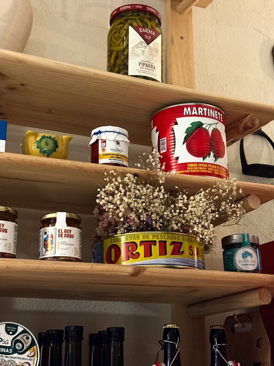 Estantes de madera que exhiben frascos y latas de diversos alimentos, incluidos pimientos y tomates.