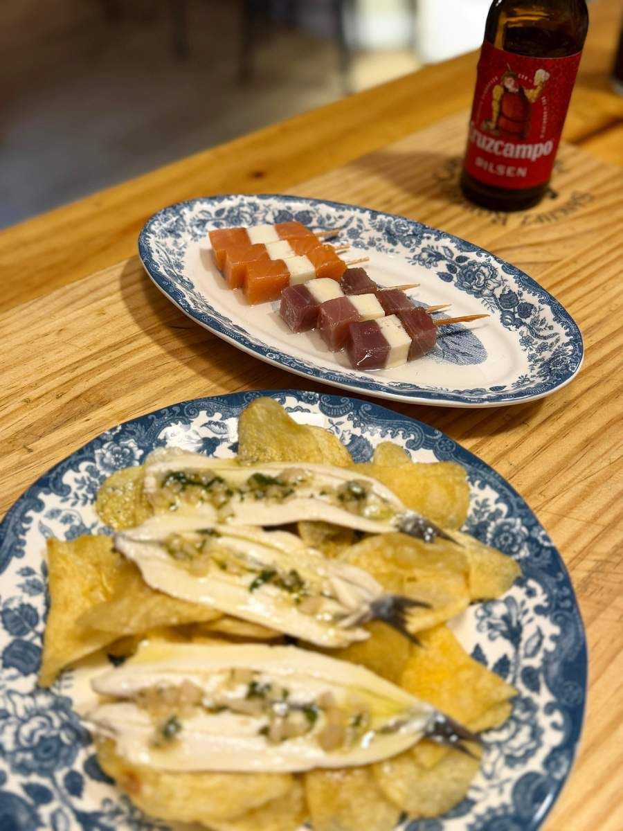 Aperitivos: brochetas, pescado frito con patatas fritas, botella de cerveza en mesa de madera.