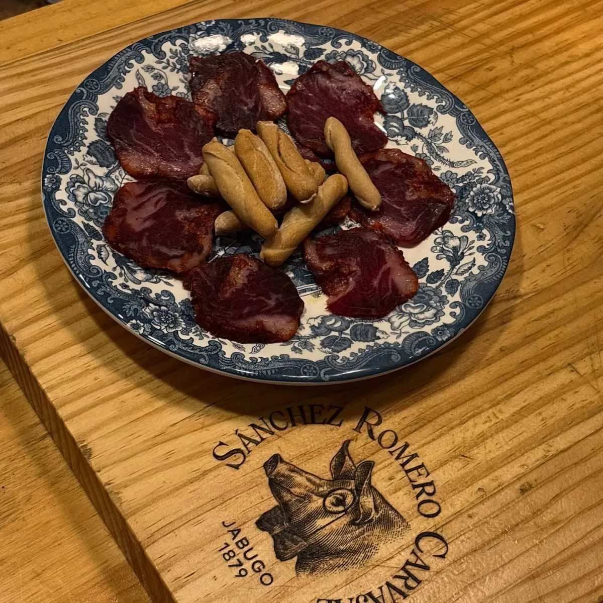Plato de carne curada en rodajas y palitos de pan sobre una tabla de servir de madera.
