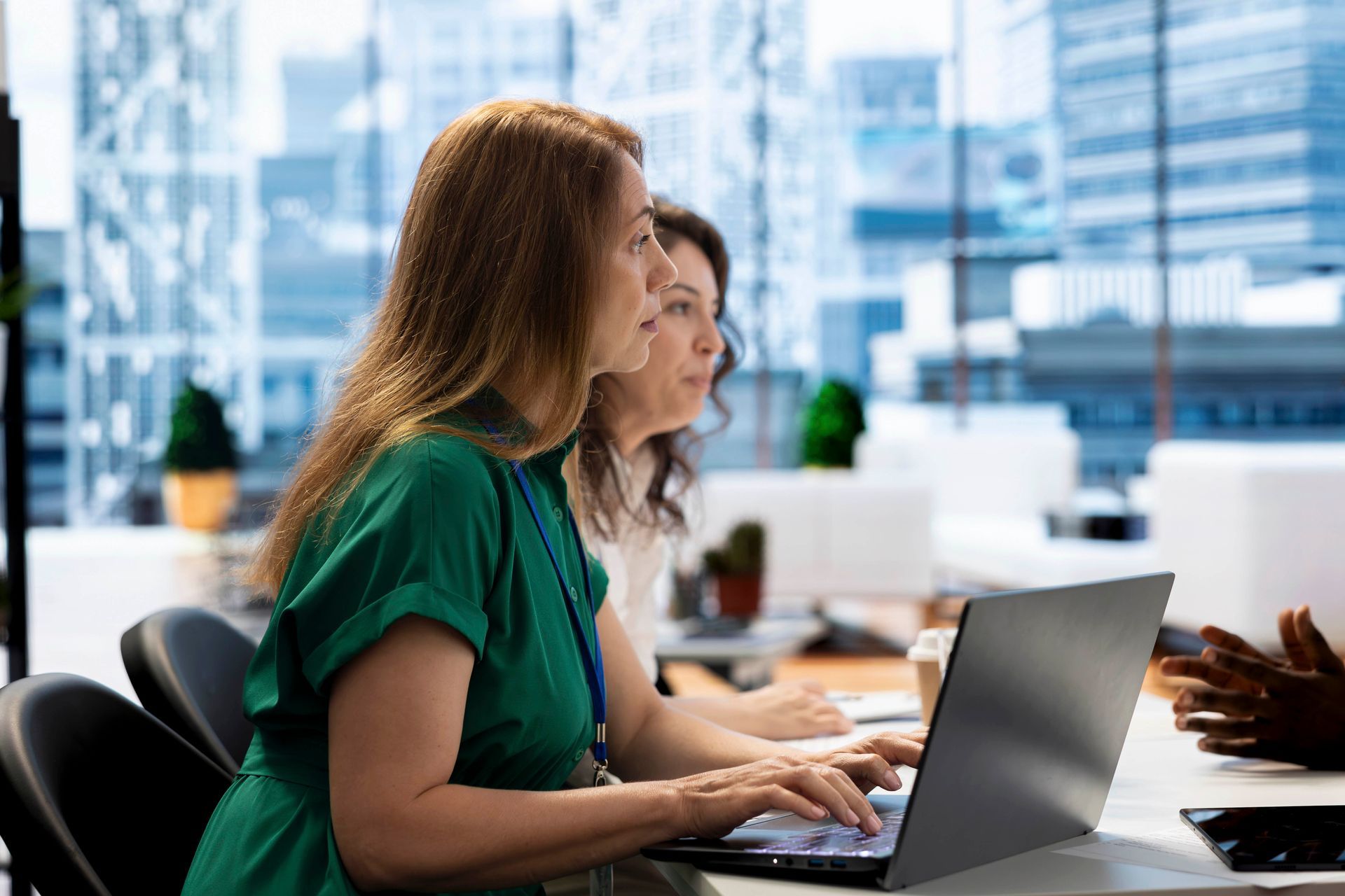 Zwei Frauen sitzen an einem Schreibtisch und benutzen einen Laptop.
