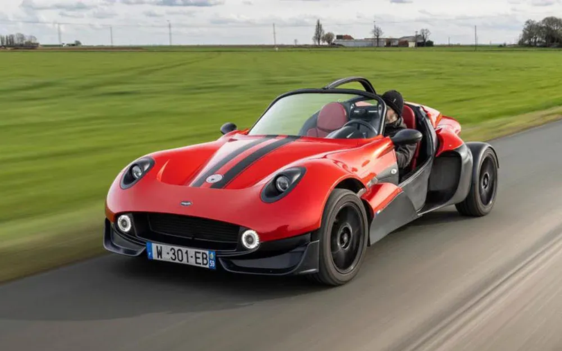 Buggy rouge roulant sur une route longeant un champ vert sous un ciel nuageux