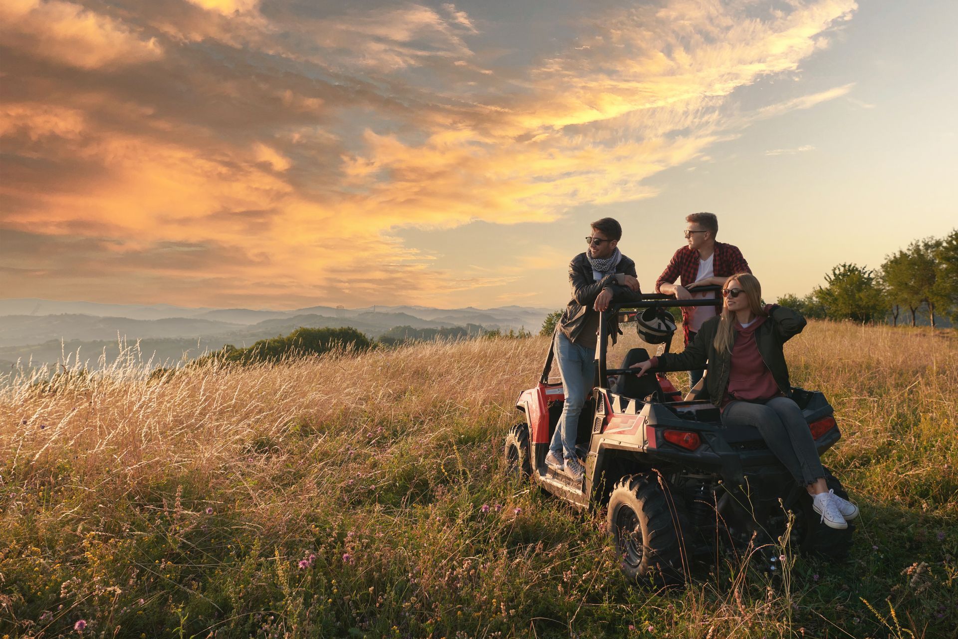 Trois personnes sur un buggy dans un champ, regardant un coucher de soleil .