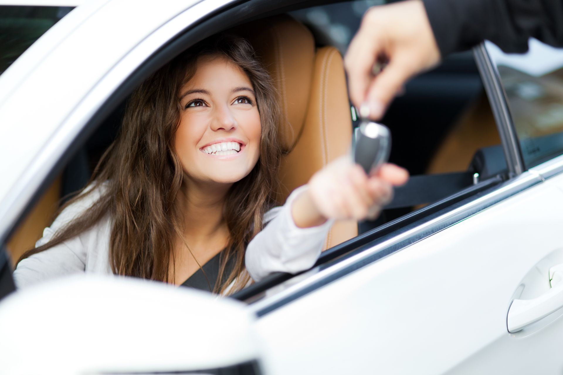 Une femme dans une voiture blanche sourit lorsqu'on lui remet les clés.