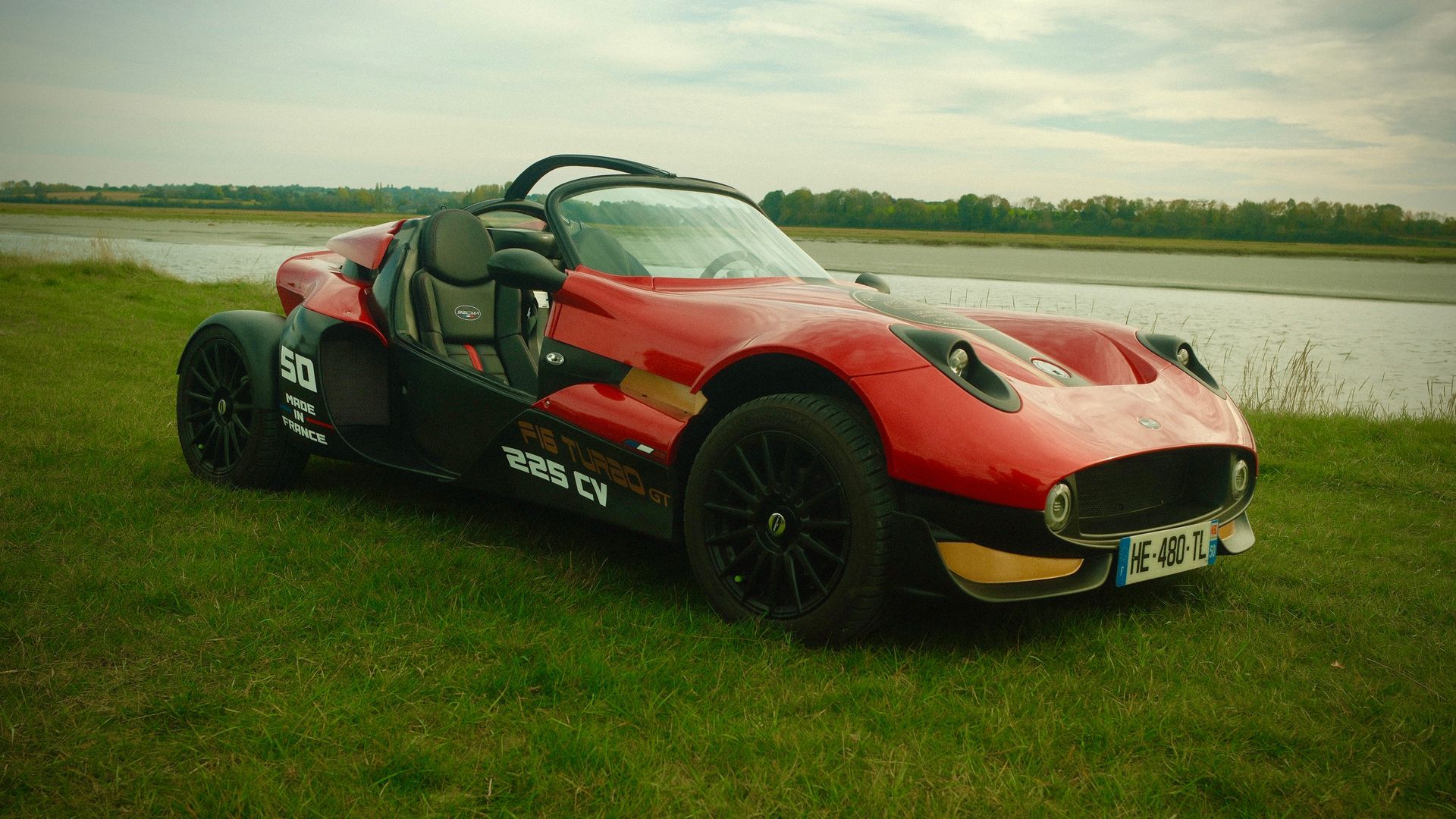 Voiture de sport rouge et noire sur l'herbe près d'un point d'eau.