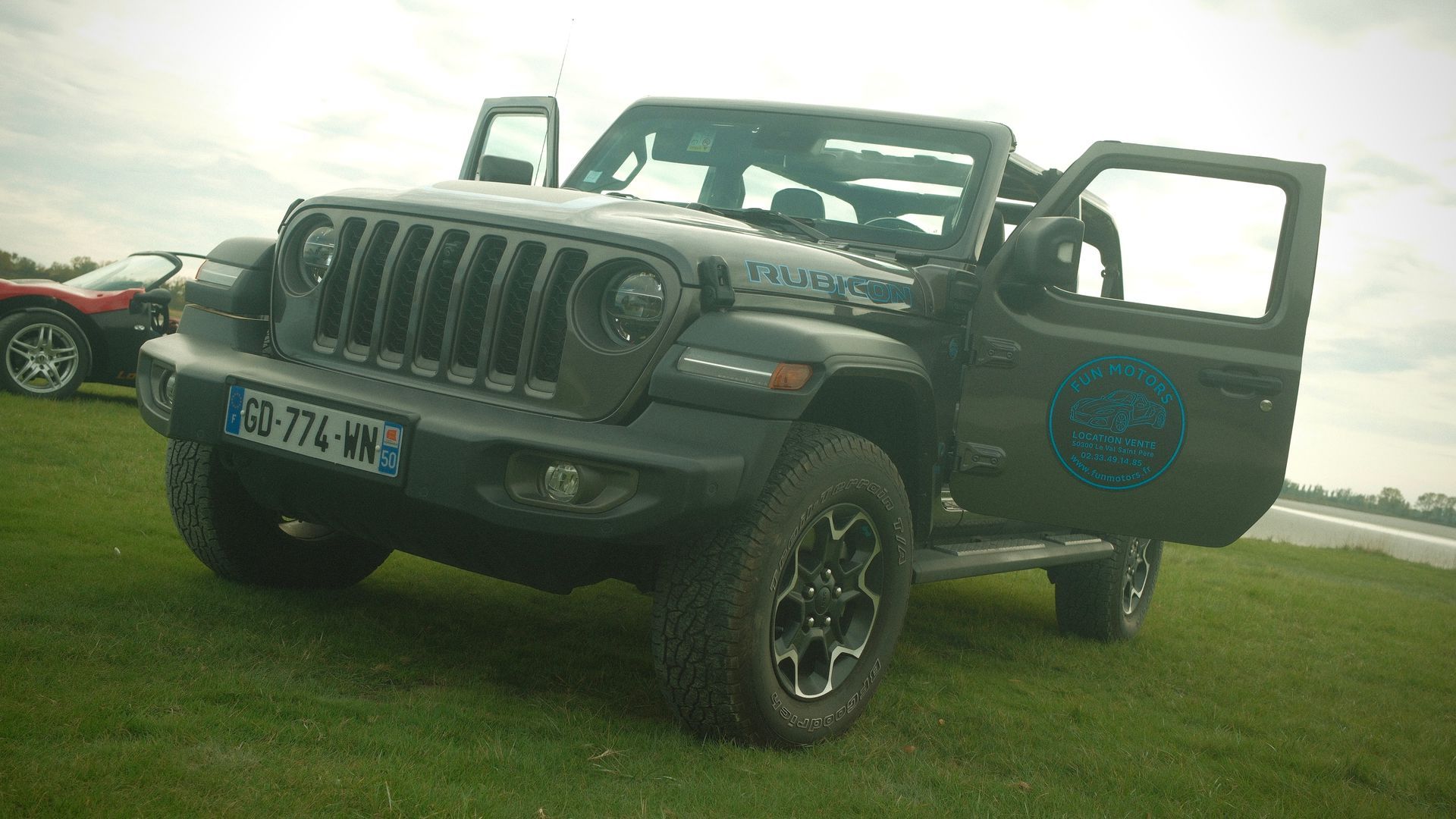 Jeep Rubicon noire garée sur l'herbe, portes ouvertes.