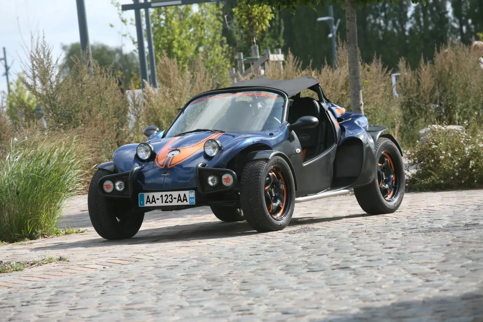 Un buggy bleu foncé à rayures orange est garé sur une route pavée près d'un espace vert.