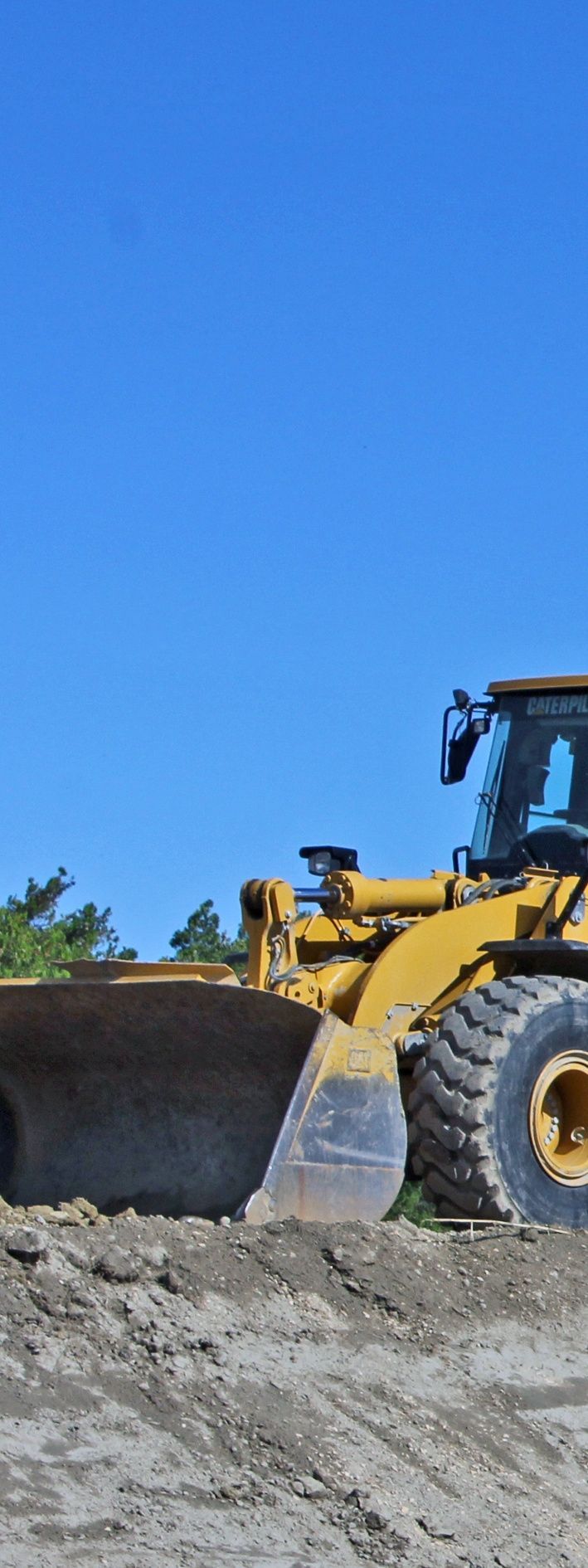Chargeuse de chantier jaune sur un tas de terre sous un ciel bleu.