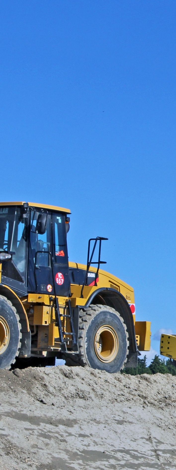 Véhicule de chantier jaune sur une colline de terre, sous un ciel bleu azur.