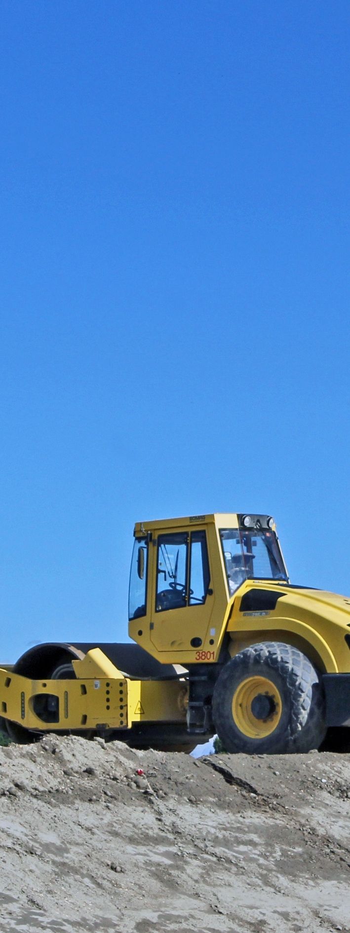 Rouleau compresseur jaune sur un sol poussiéreux sous un ciel d'un bleu éclatant.