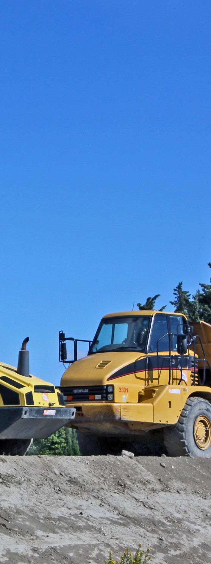 Véhicule de chantier jaune sur une colline de terre sous un ciel bleu.