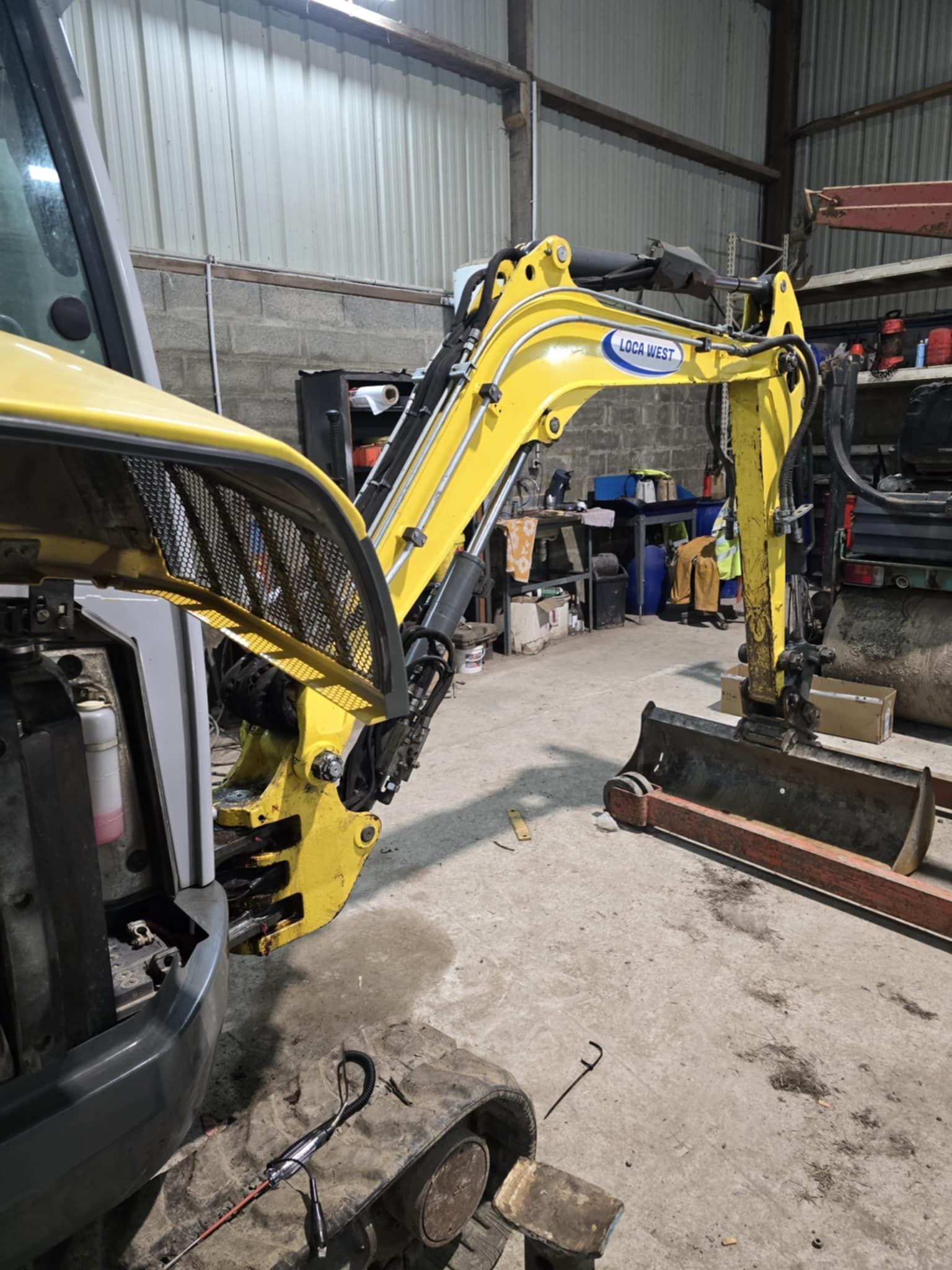 Le bras d'une excavatrice jaune est déployé dans un garage