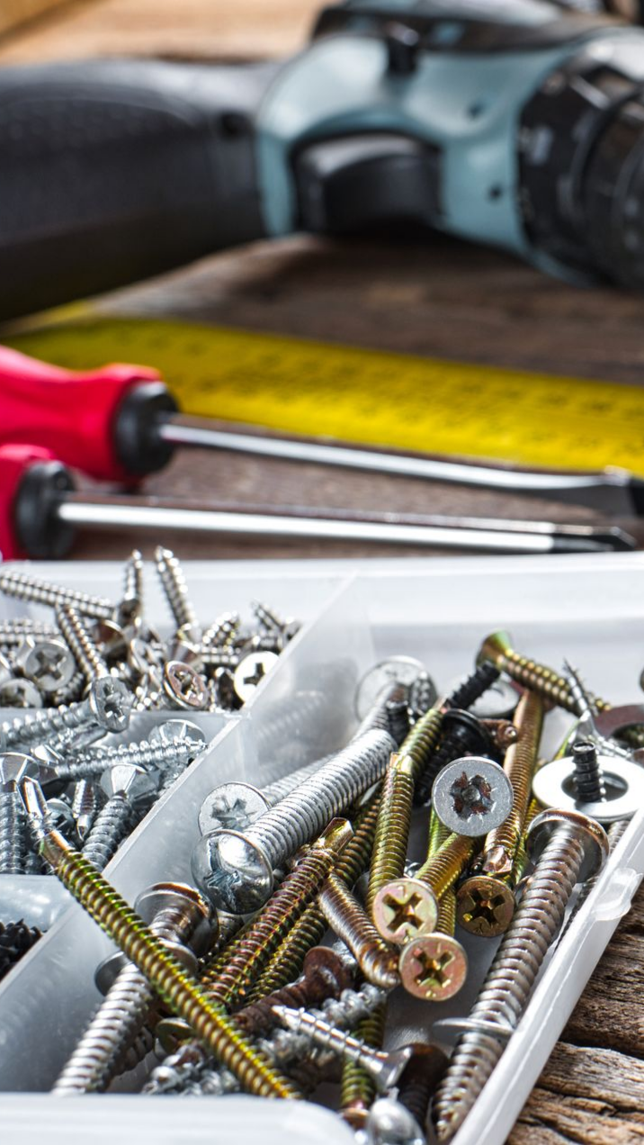 Des vis, une boîte à outils et des tournevis, avec une perceuse en arrière-plan