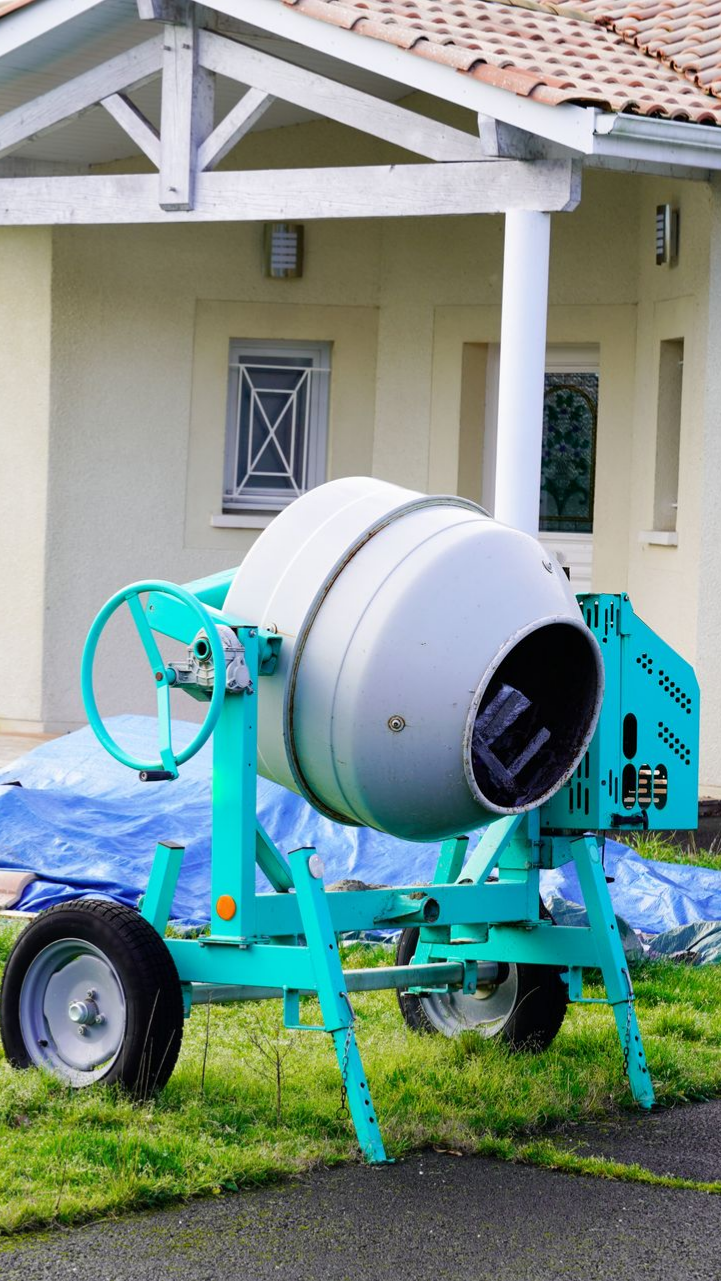 Une bétonnière turquoise et grise sur une pelouse devant une maison