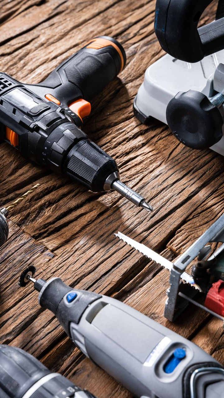Outils électriques disposés sur une surface en bois : perceuse, outil rotatif, scie et meuleuse