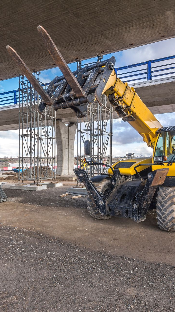 Chariot élévateur jaune à fourches déployées près d'un chantier de construction de pont