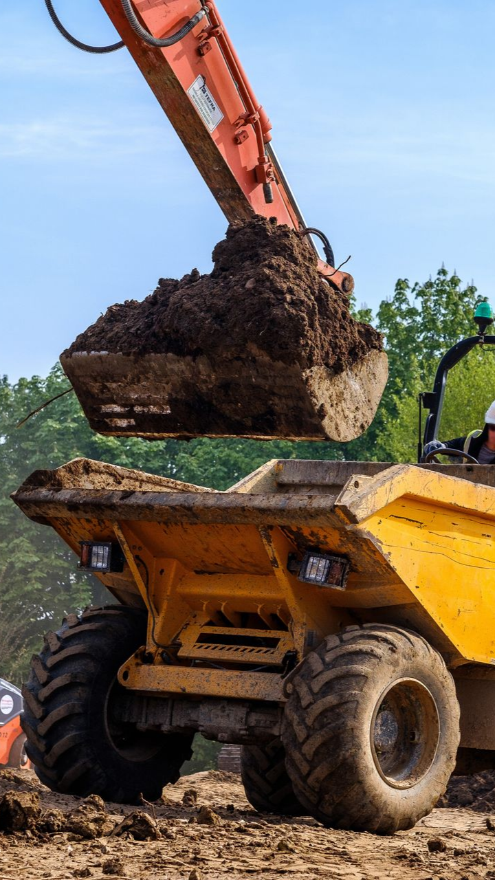 Une excavatrice déverse de la terre dans un camion-benne jaune sur un chantier de construction