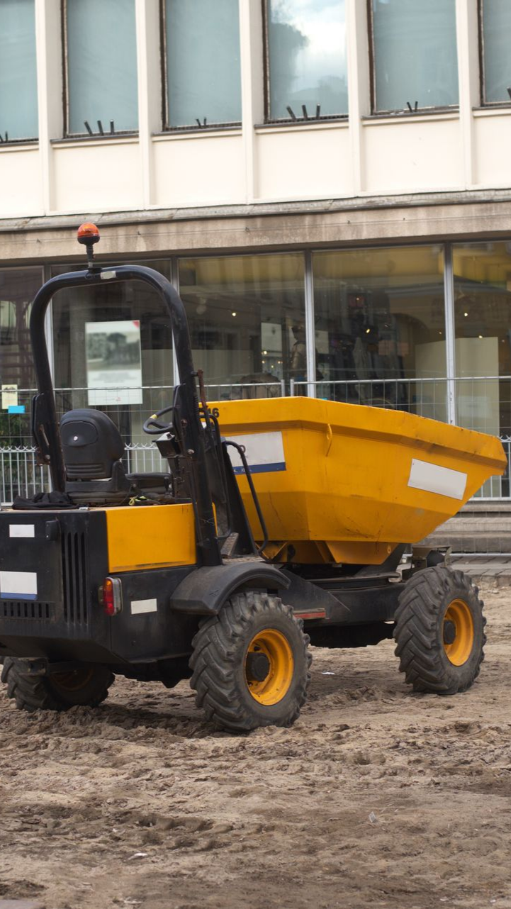 Camion-benne de chantier jaune et noir sur un sol en terre battue 