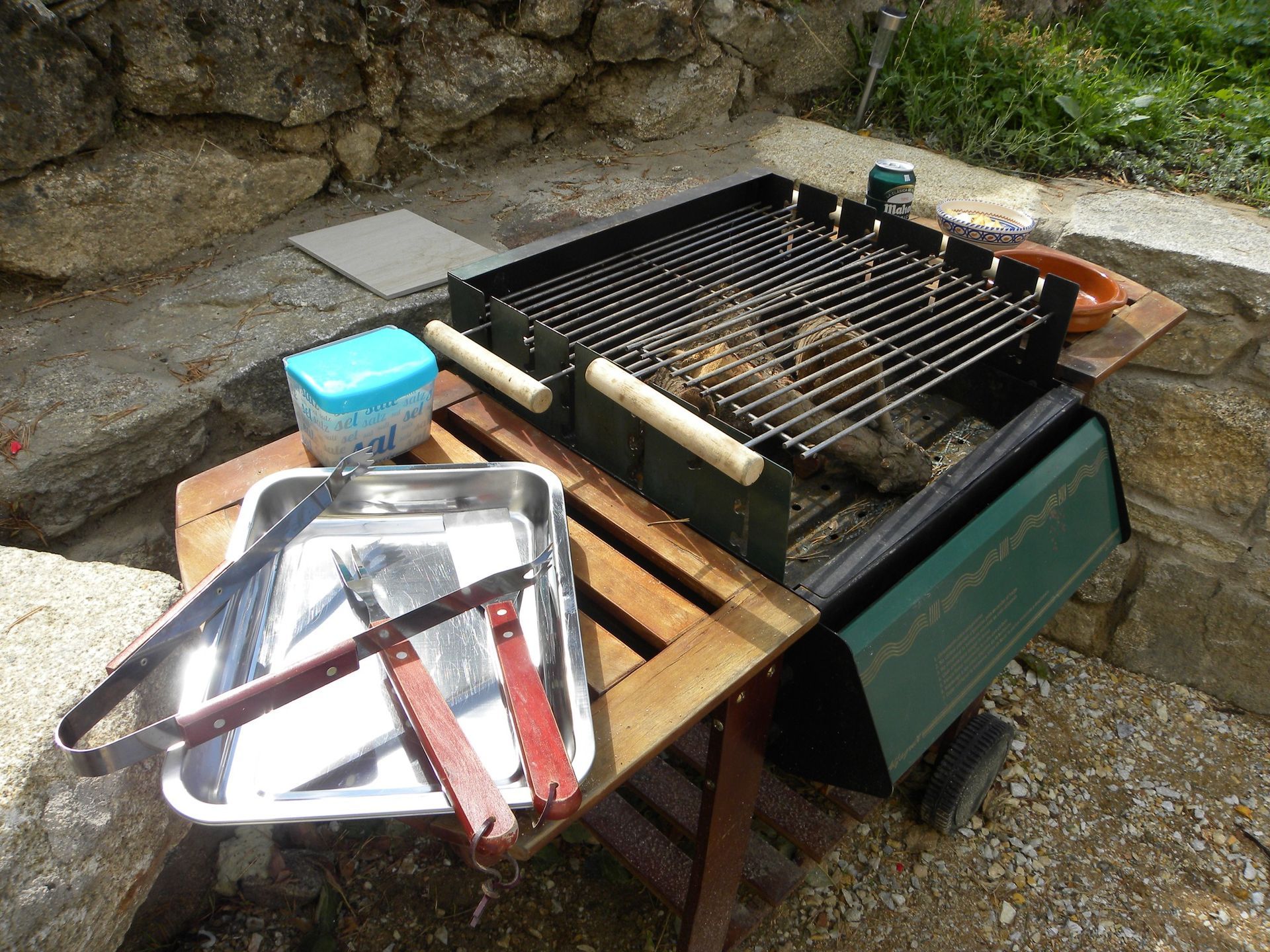 Hay una parrilla sobre una mesa de madera junto a una bandeja de pinzas.