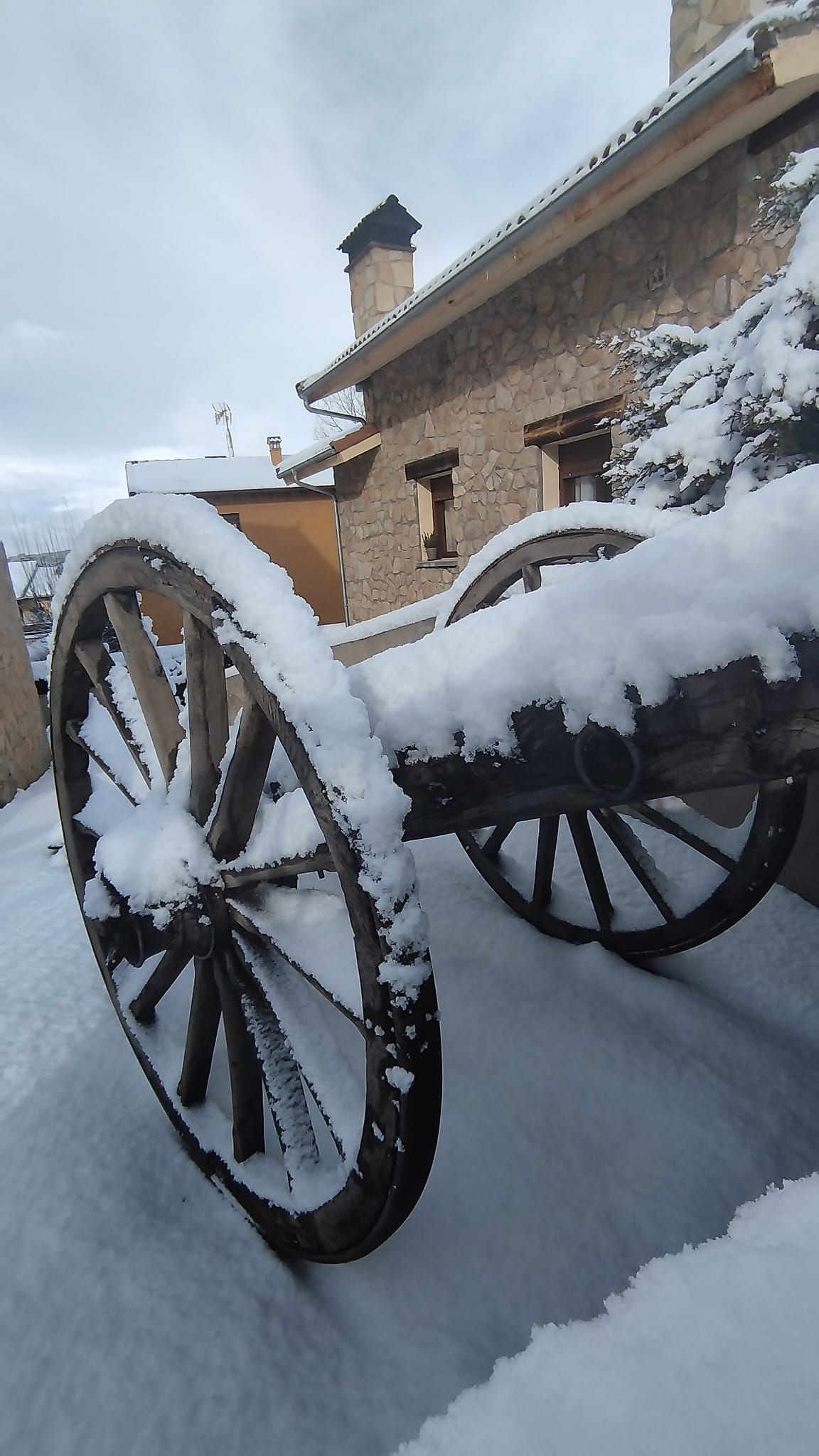 Una rueda de carro está cubierta de nieve frente a un edificio.