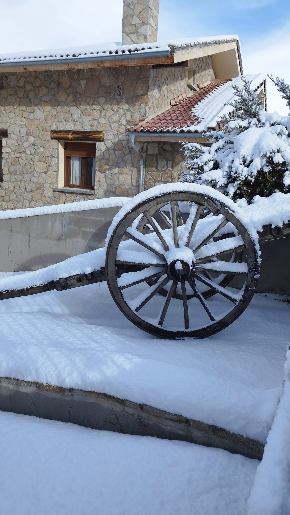 Una rueda de madera está cubierta de nieve delante de un edificio de piedra.