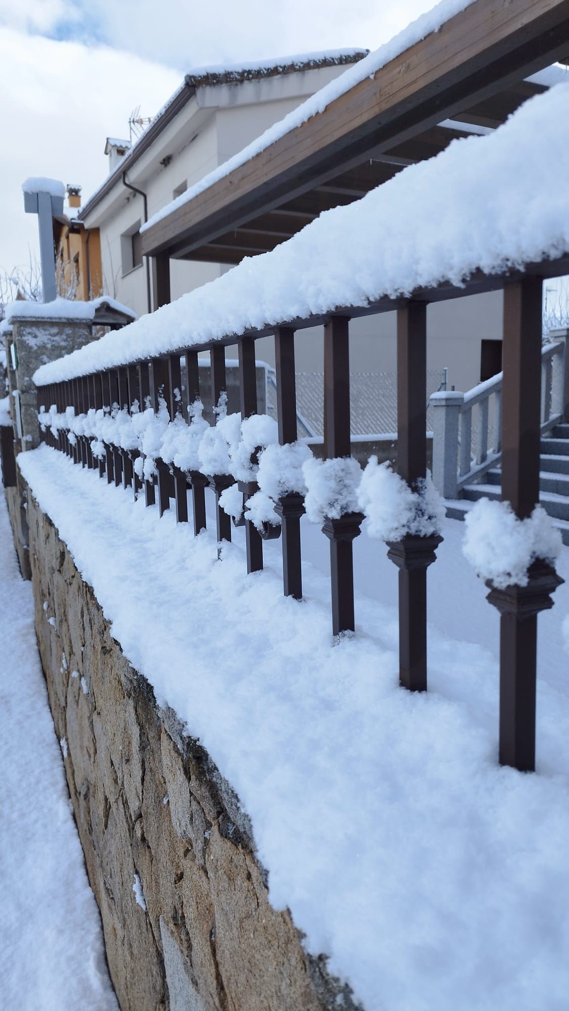 Una valla nevada con un muro de piedra al fondo