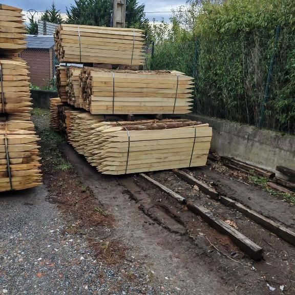 Pilas de postes de madera puntiagudos sobre tierra y vigas de madera, al aire libre.